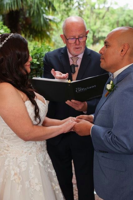 Andy Uhlig officiating a garden wedding ceremony, reading from The Officiant book as the couple exchange rings