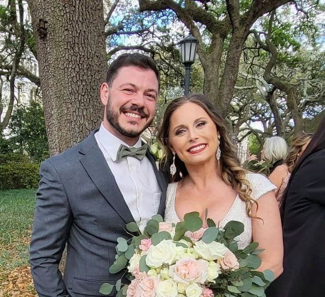 Rebecca and Adam beaming on their wedding day beneath Savannah live oaks, bride holding a lush bouquet of white and blush roses with eucalyptus
